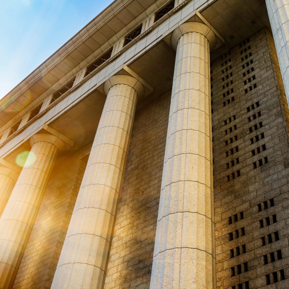 Sunlight streaming through tall stone columns of a grand neoclassical building.